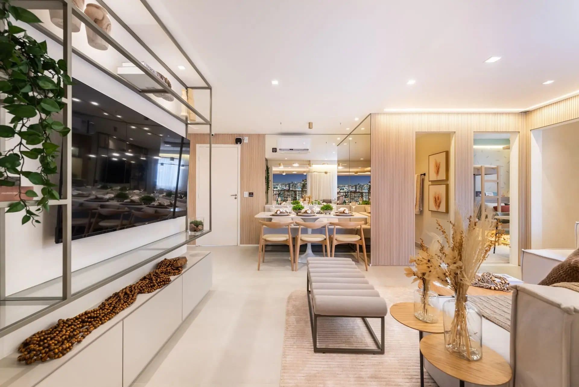 Sala de estar e jantar integrada com decoração em tons neutros, painel ripado e estante metálica vazada.