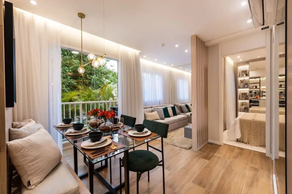 Sala de jantar integrada com mesa de vidro, cadeiras estofadas e vista para área verde.