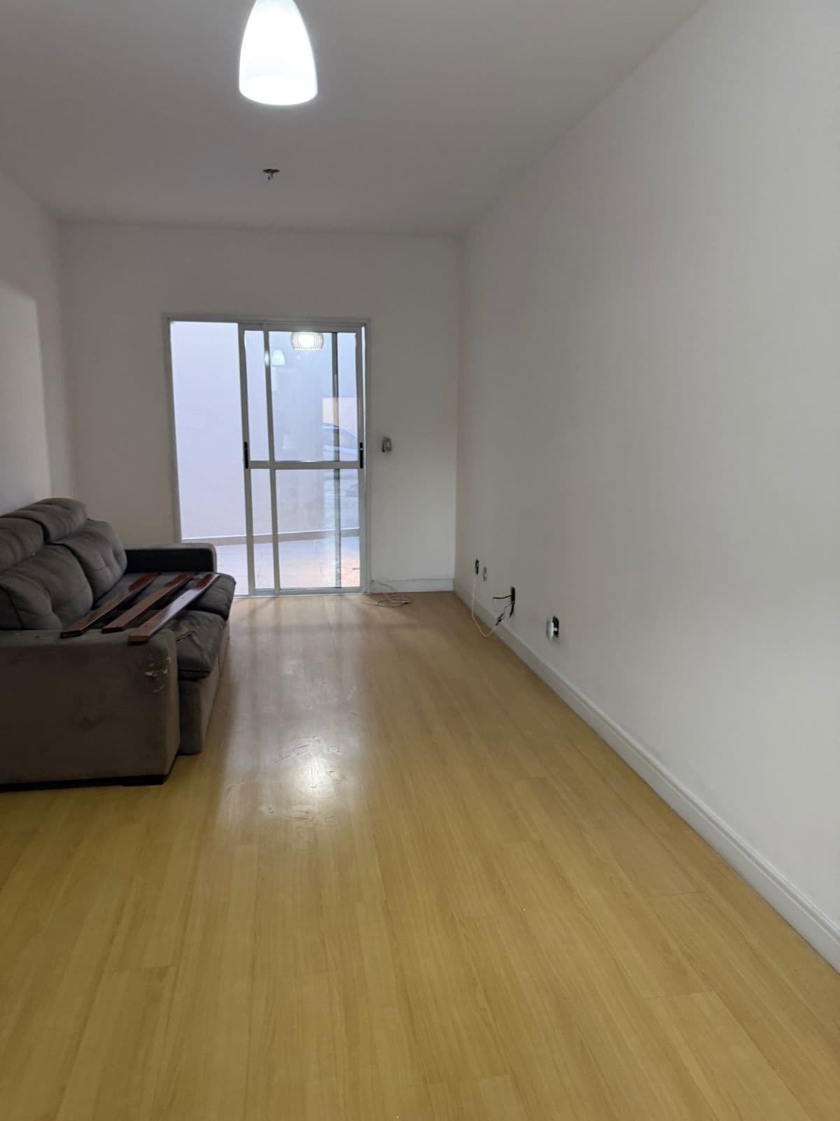 Sala de estar com piso amadeirado, paredes brancas e porta de vidro de correr com acesso externo.